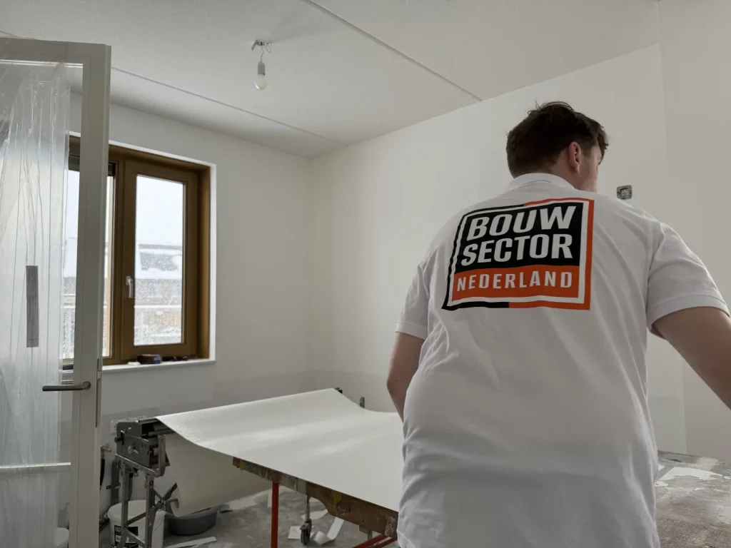 Behanger van Bouwsector Nederland met een baan vliesbehang op de plaktafel in een lege kamer