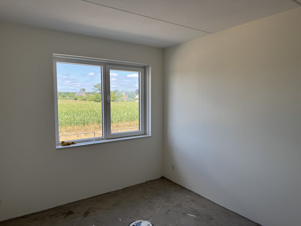 Lege nieuwbouwslaapkamer met gladde lichte wanden en een raam met uitzicht over het veld