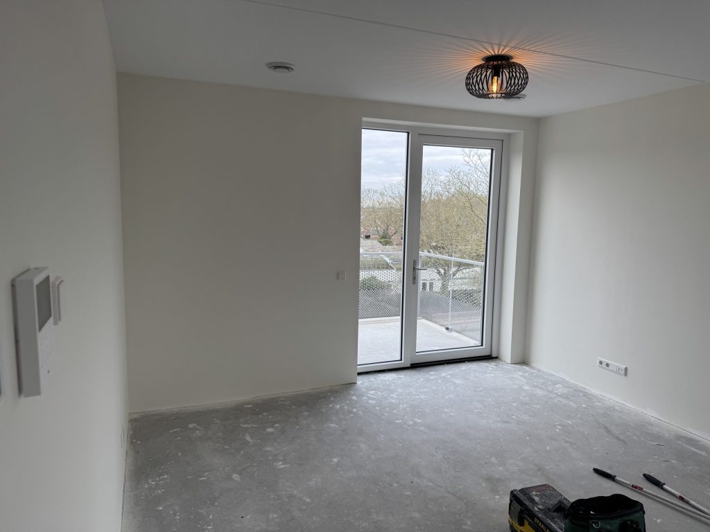 Lege nieuwe appartementkamer met balkondeuren en kale lichte wanden, kort na de oplevering